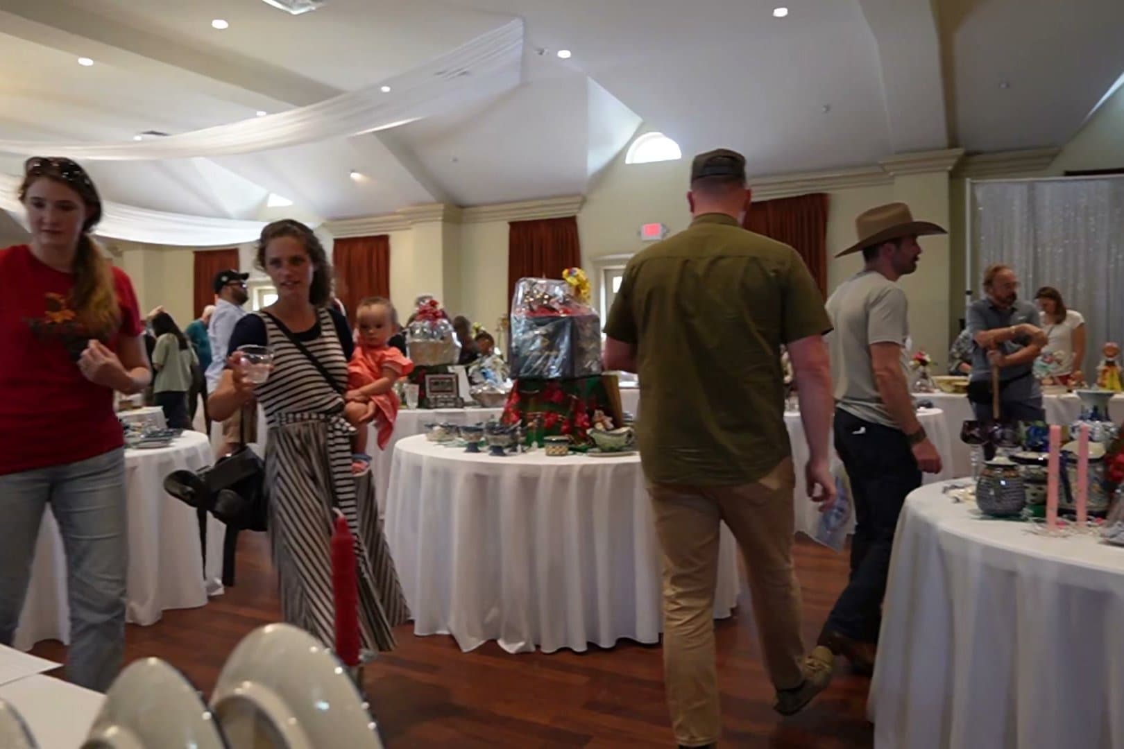 Visitors moving between the auction tables in the parish hall, reading bid sheets as they go.
