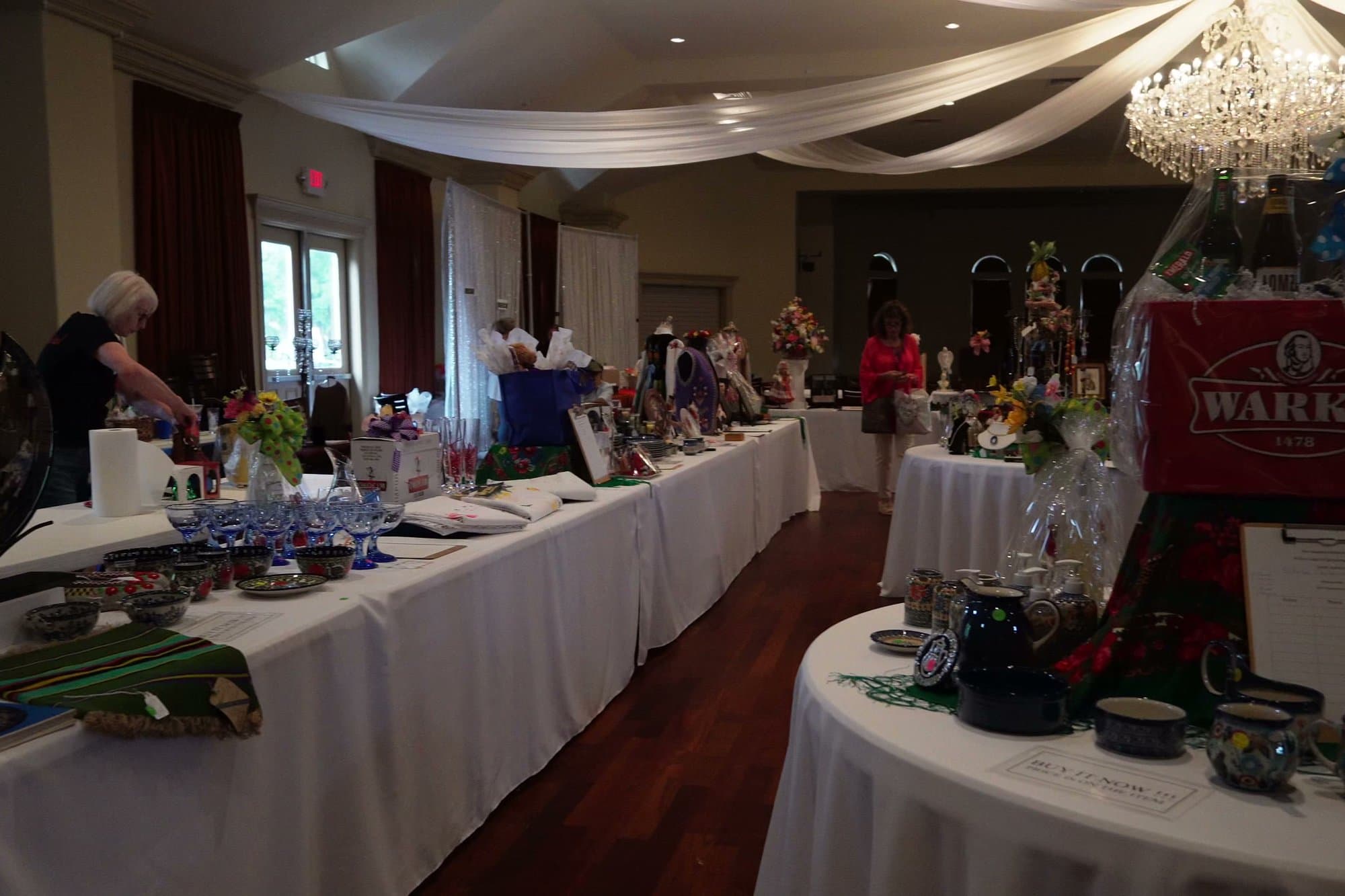 Round tables across the parish hall, each covered in a white cloth and crowded with auction lots under the chandeliers.