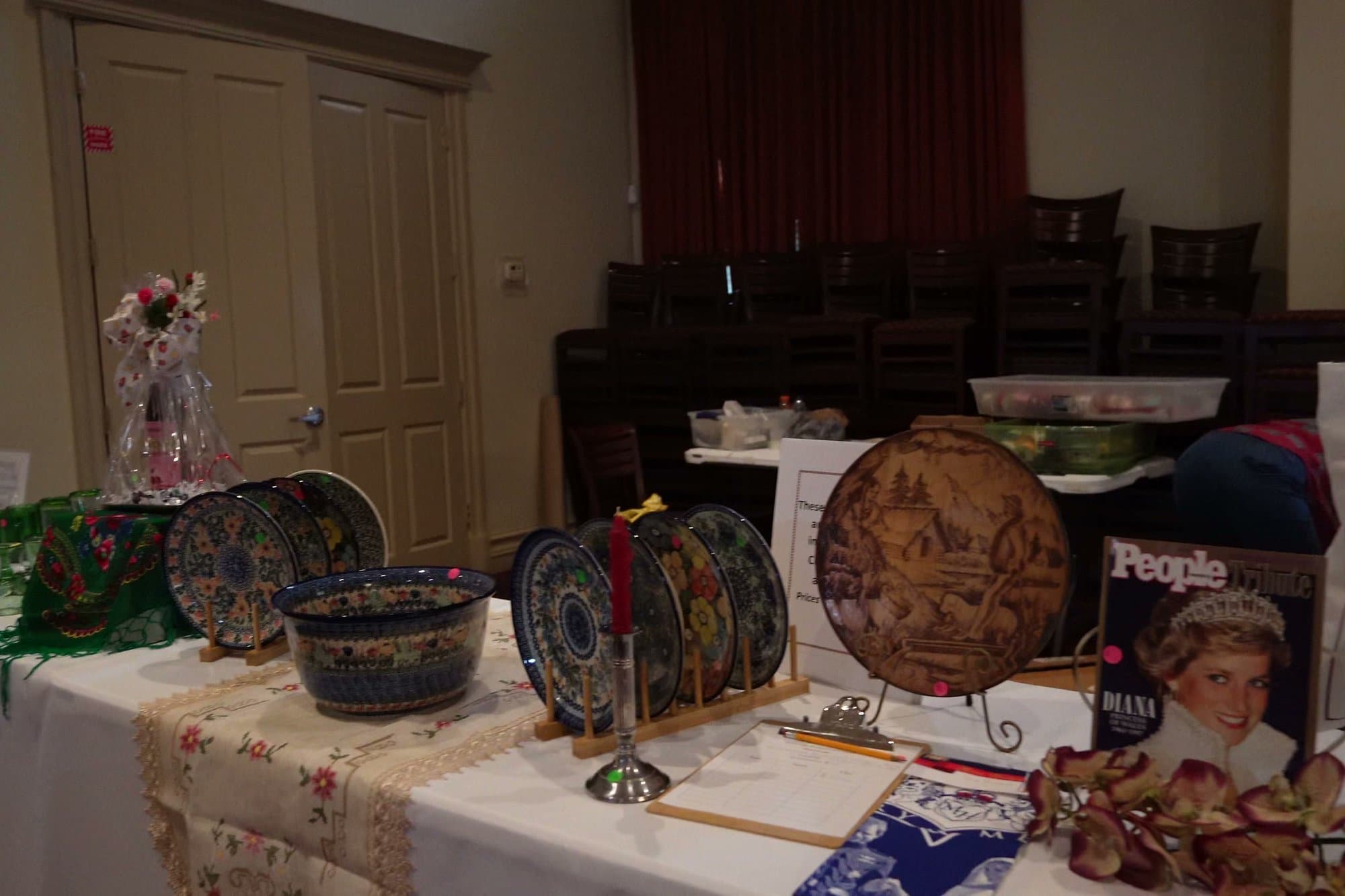 A long auction table laid with hand-painted Bolesławiec stoneware, framed pictures, glassware and an embroidered cloth.
