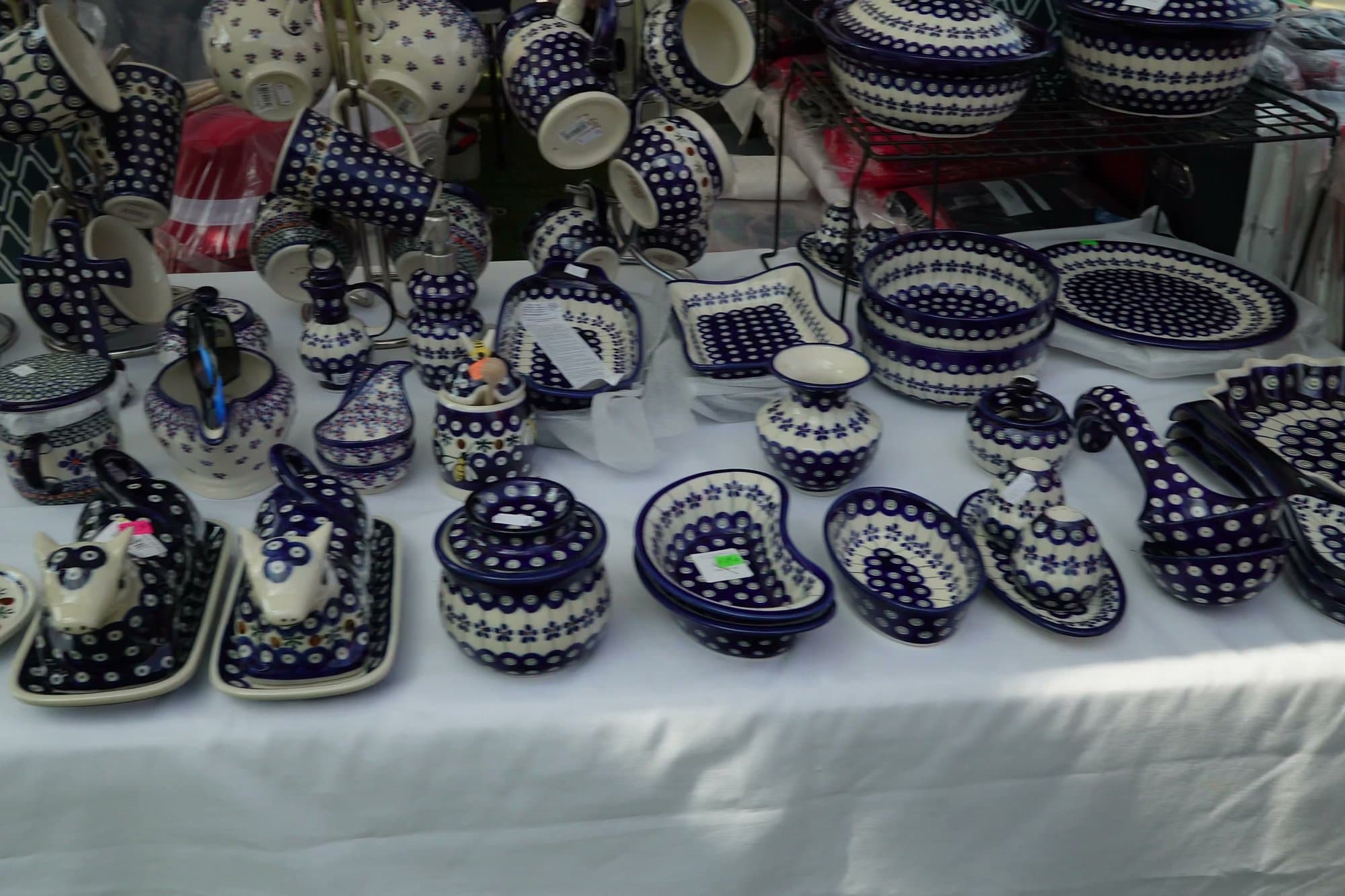 A stall table covered in hand-painted Bolesławiec stoneware — bowls, plates, jugs and baking dishes in cobalt blue and white peacock-eye patterns.