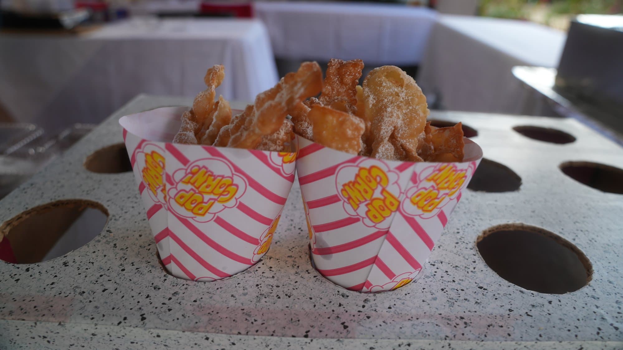 Two red and white striped cartons filled with fried pastry dusted heavily in powdered sugar, standing on a speckled counter.